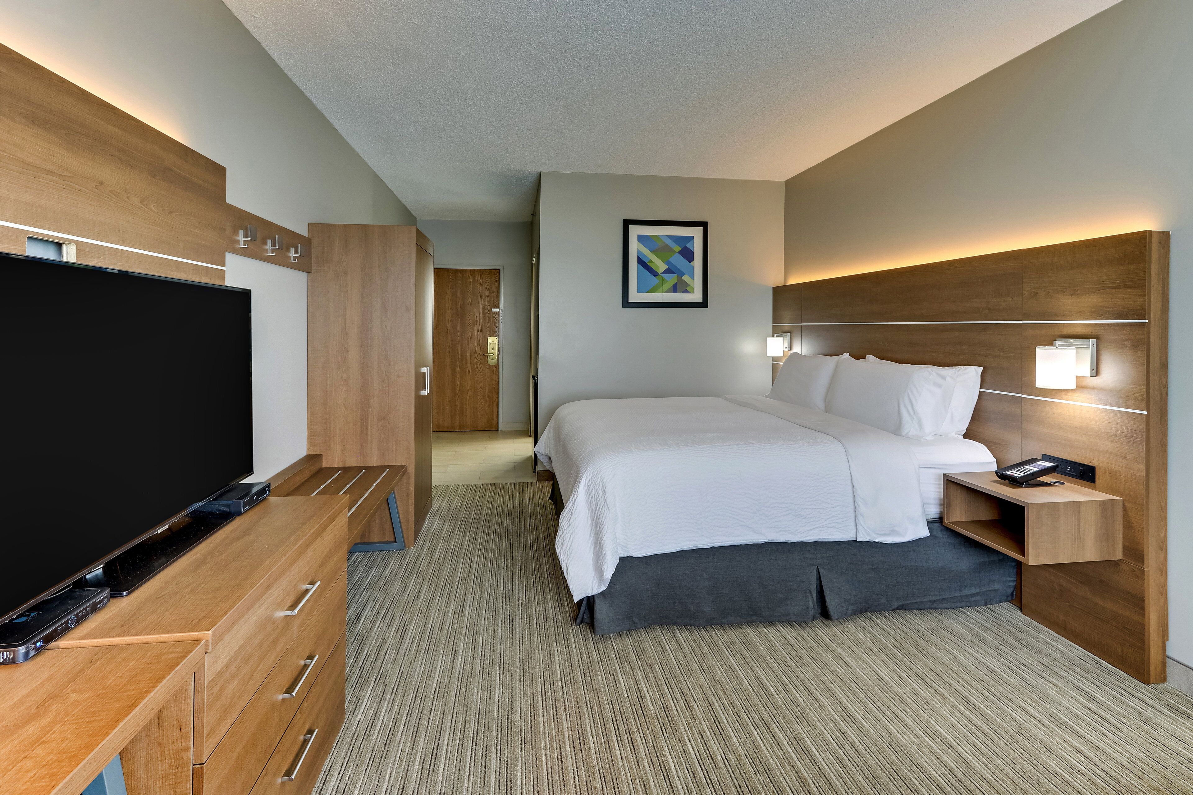 Een moderne hotelkamer met een grote flatscreen-tv, houten meubels, een netjes opgemaakt bed en een ingelijst schilderij aan de muur.