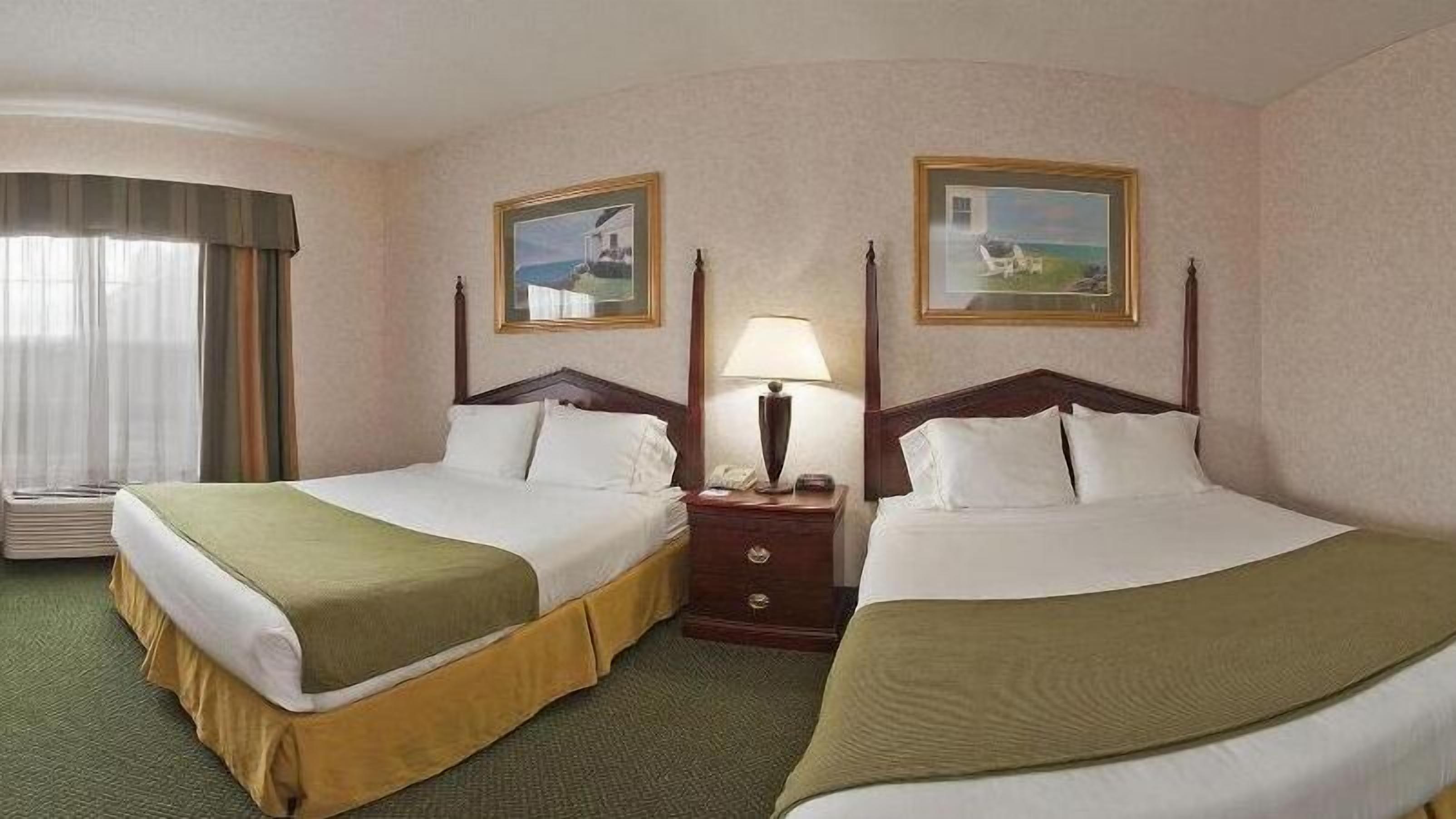 Habitación de hotel con dos camas, una mesita de noche con lámpara y dos cuadros en las paredes.