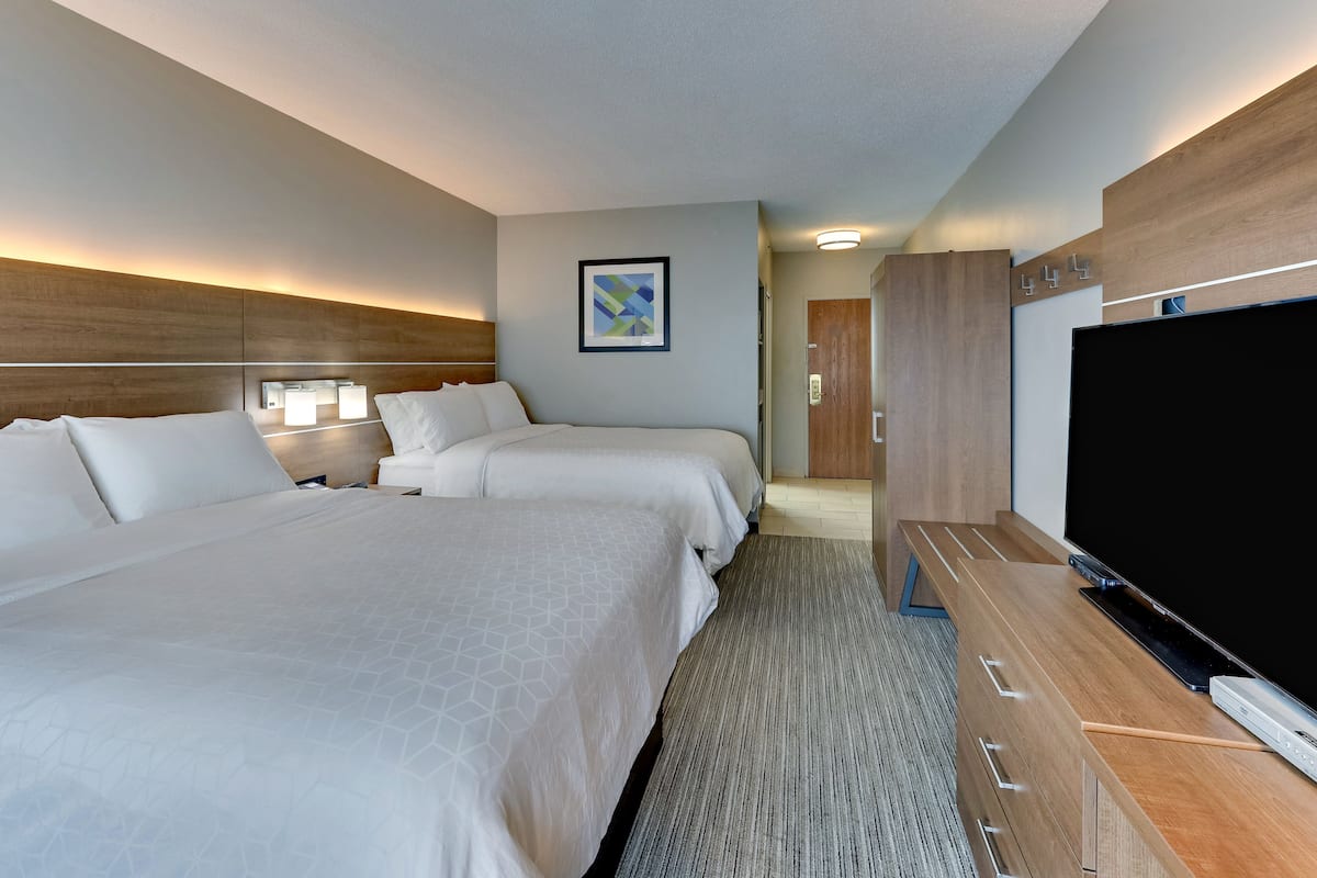 A hotel room with two beds, a flat-screen TV, a wooden dresser, and a framed abstract painting on the wall.