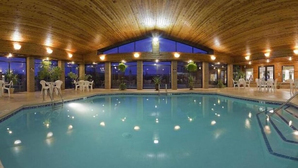 An indoor swimming pool with clear blue water, surrounded by wooden walls and ceiling, and furnished with white chairs and tables. - Holiday Inn Express Hotel & Suites Bad Axe by IHG (Bad Axe)