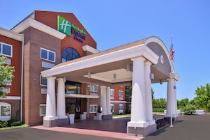 Un hotel Holiday Inn Express & Suites con entrada cubierta e una bandera estadounidense.