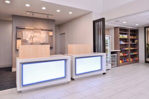 Zona de recepción de un hotel con diseño moderno, que incluye un mostrador de recepción, un minibar y un bar de aperitivos.
