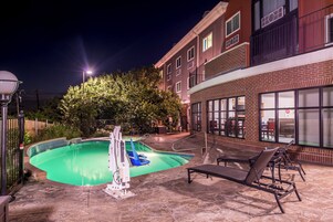 Zona de piscina con trampolín, sillas de descanso y un edificio de ladrillo con grandes ventanales.