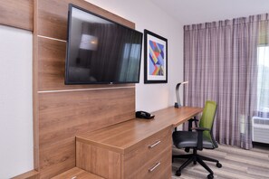 A hotel room with a wooden desk, a flat-screen TV mounted above it, a framed abstract art piece, a green office chair, and a window with curtains. - Holiday Inn Express Hotel & Suites Elgin by IHG (Elgin)
