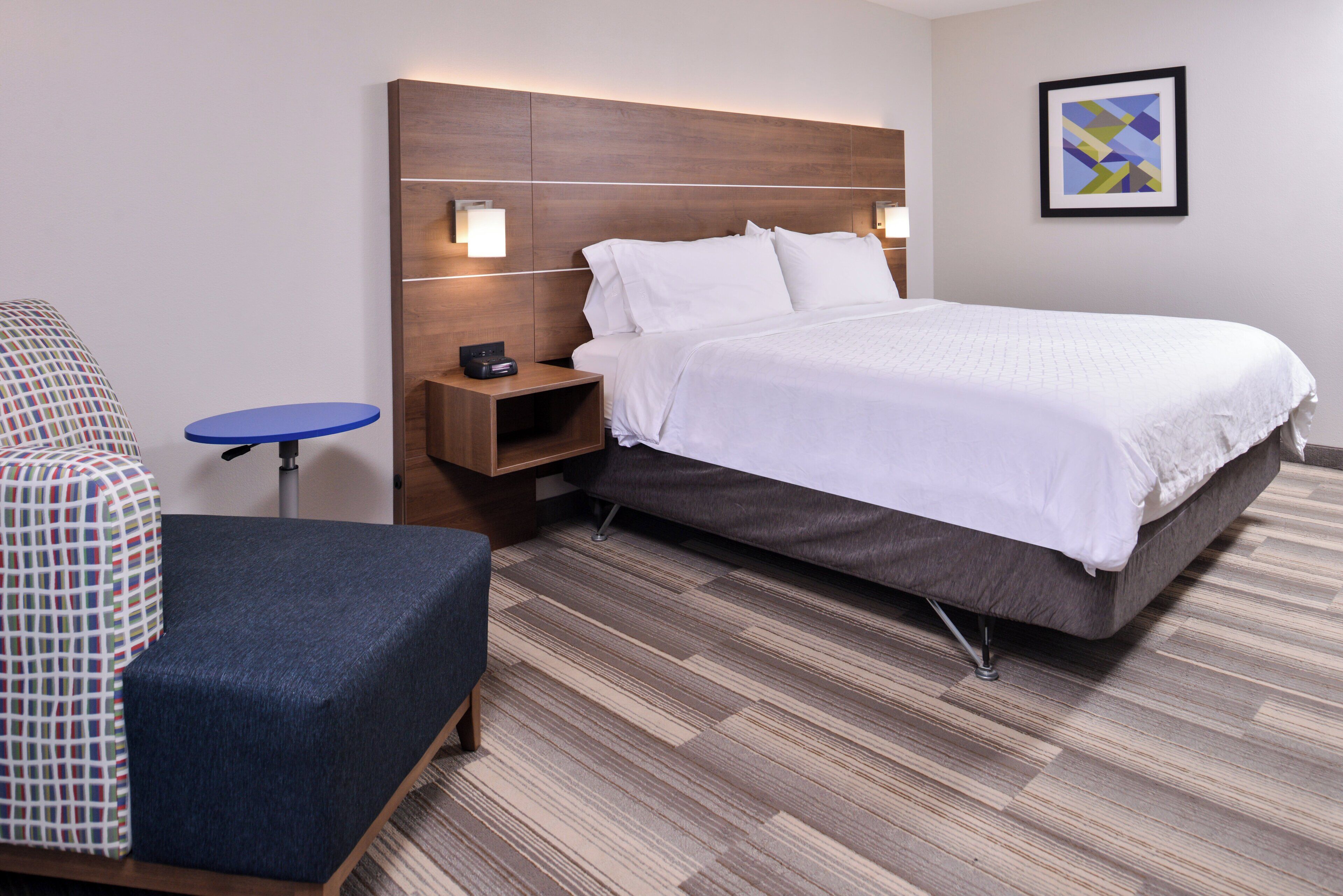 A hotel room with a bed, a chair, a small table, and a nightstand.