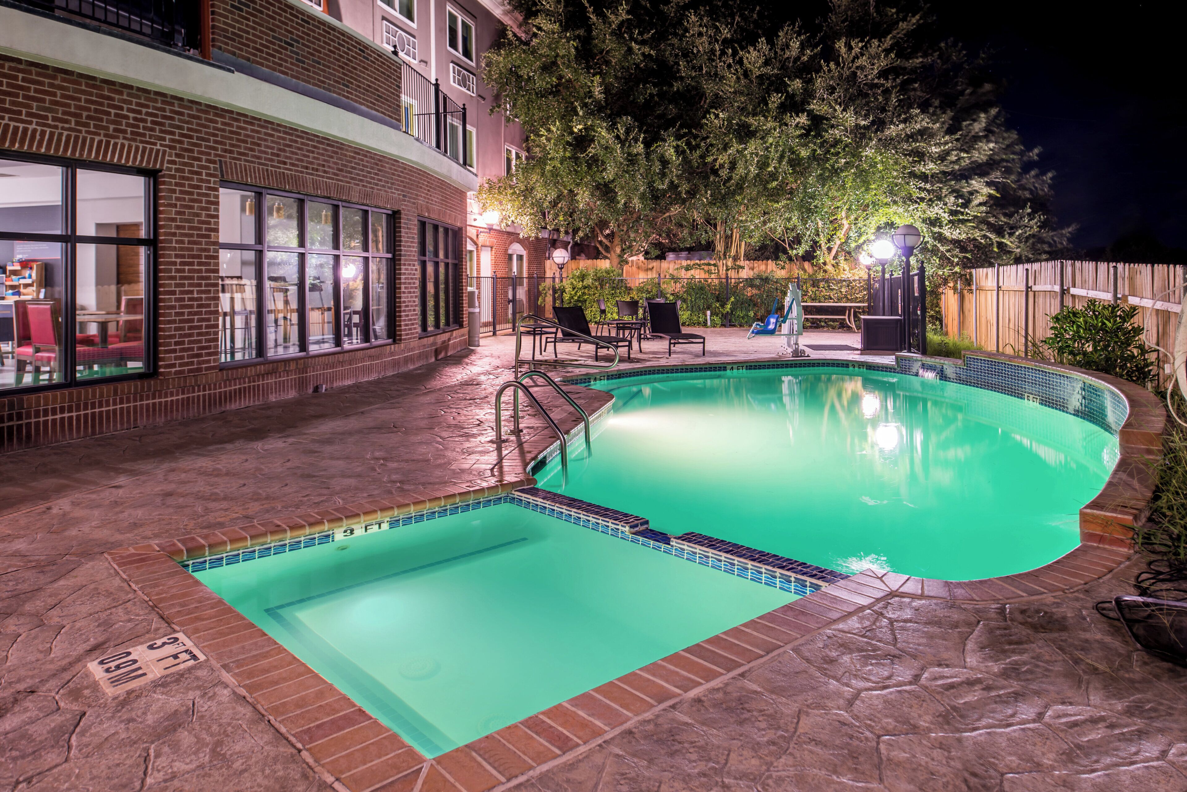 Una piscina con borde de azulejos, rodeada por un patio de ladrillo y una valla de madera.