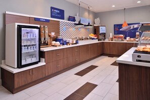 A modern breakfast area with a refrigerator stocked with beverages, a coffee machine, and a variety of food items on the counter. - Holiday Inn Express Hotel & Suites Elgin by IHG (Elgin)