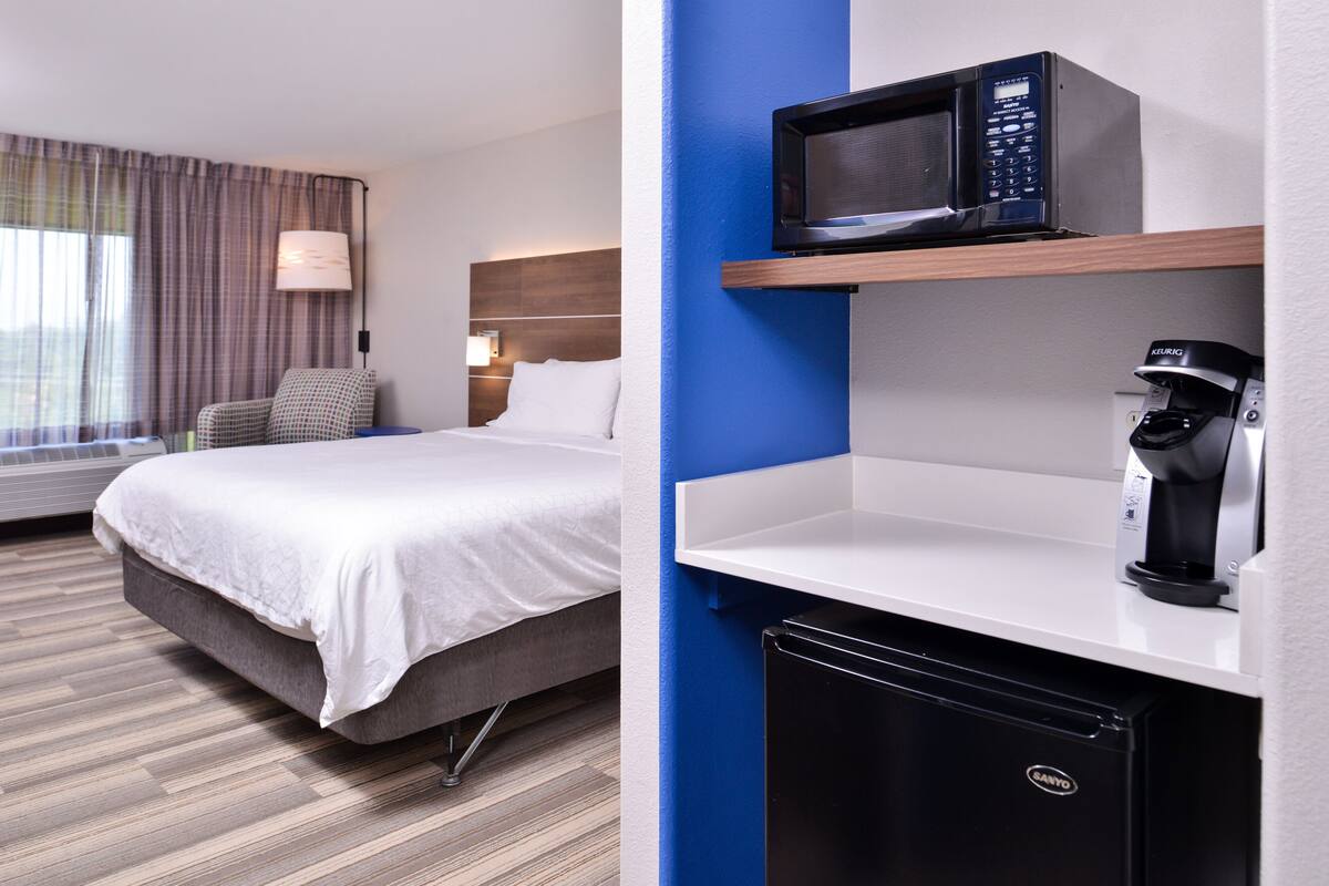 A hotel room with a bed, a desk with a microwave, and a coffee machine.