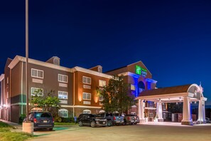 A hotel with a prominent green sign, multiple parking spaces, and a well-lit entrance.