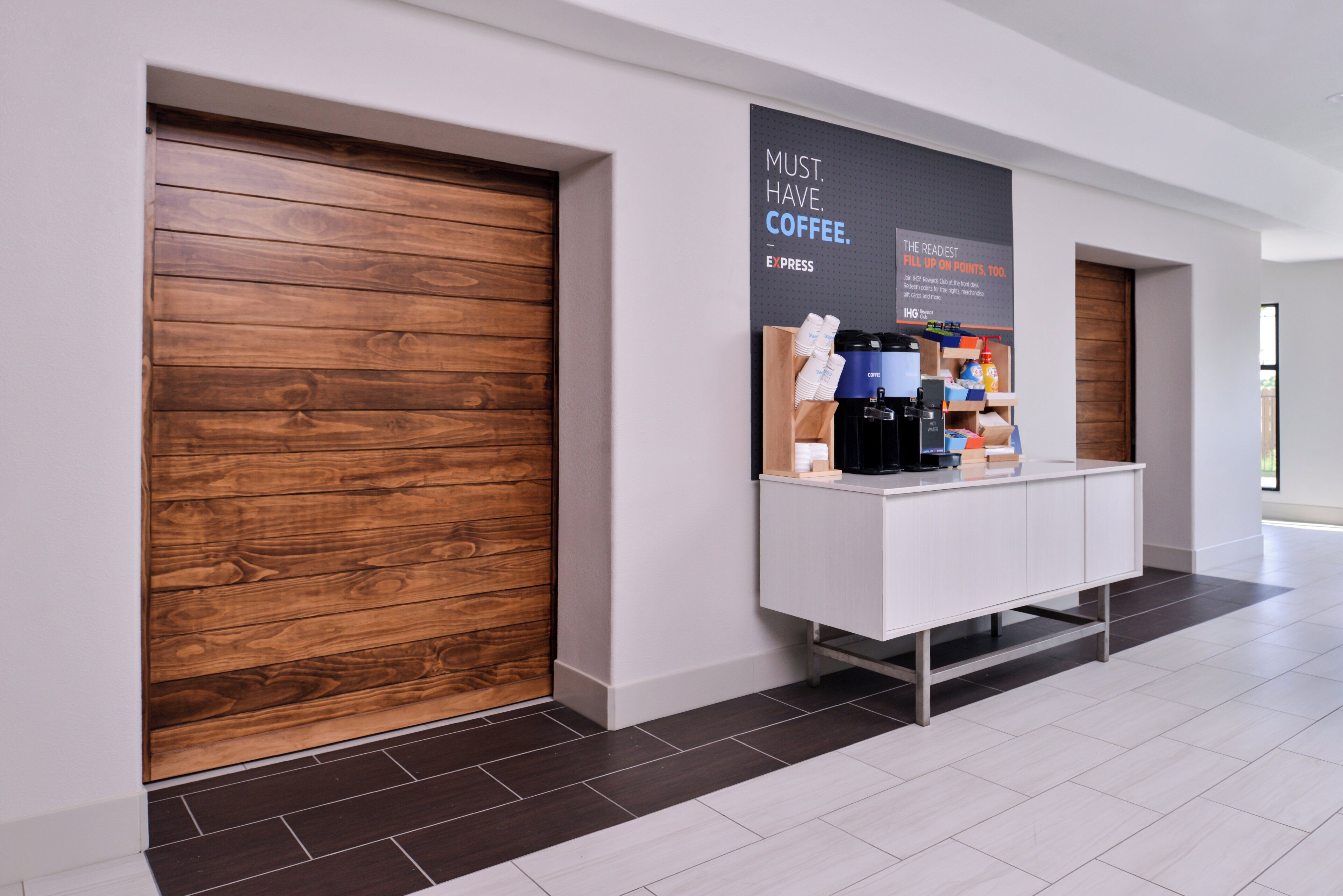 Un moderno vestíbulo de hotel con una estación de café, paneles de madera en las paredes y piso de baldosas.