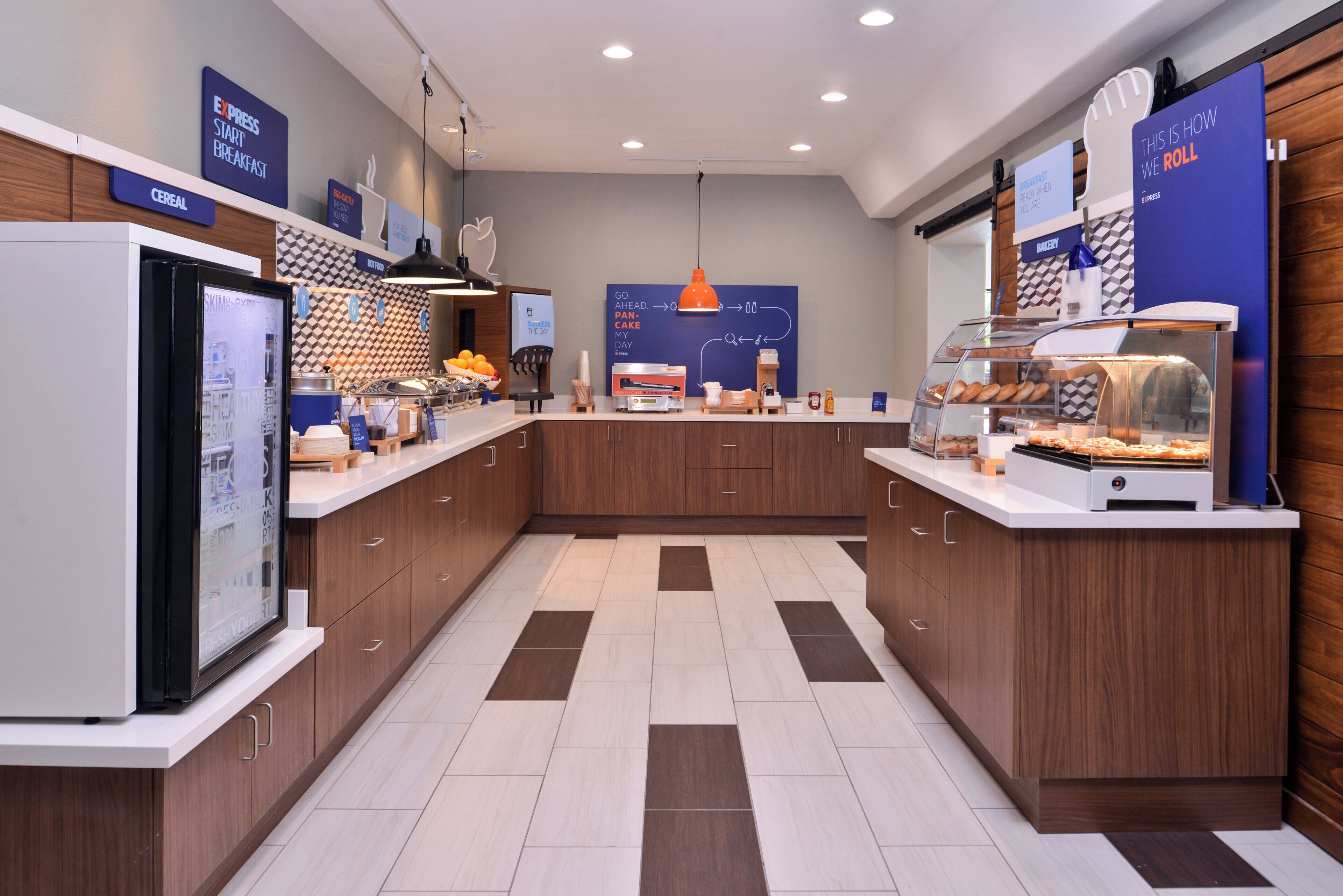 A modern breakfast area with a self-serve station, a display case with pastries, and a counter with a coffee machine.