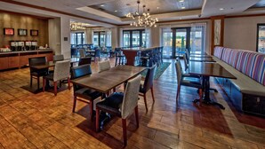 Ein geräumiger Hotel-Speisesaal mit mehreren Tischen und Stühlen, einer langen Theke mit Kaffeemaschinen und großen Fenstern, die für natürliches Licht sorgen.