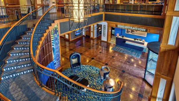 Eine beeindruckende, mehrstöckige Hotelhalle mit einer zentralen Wendeltreppe, einer Rezeption und einer Sitzecke mit gemustertem Teppich.