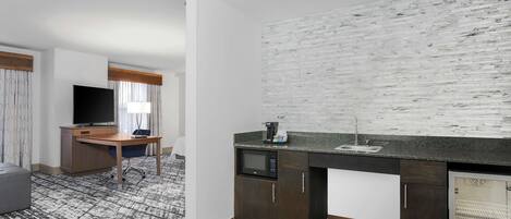 A compact living space with a kitchenette, a flat-screen TV, a desk, and a seating area.