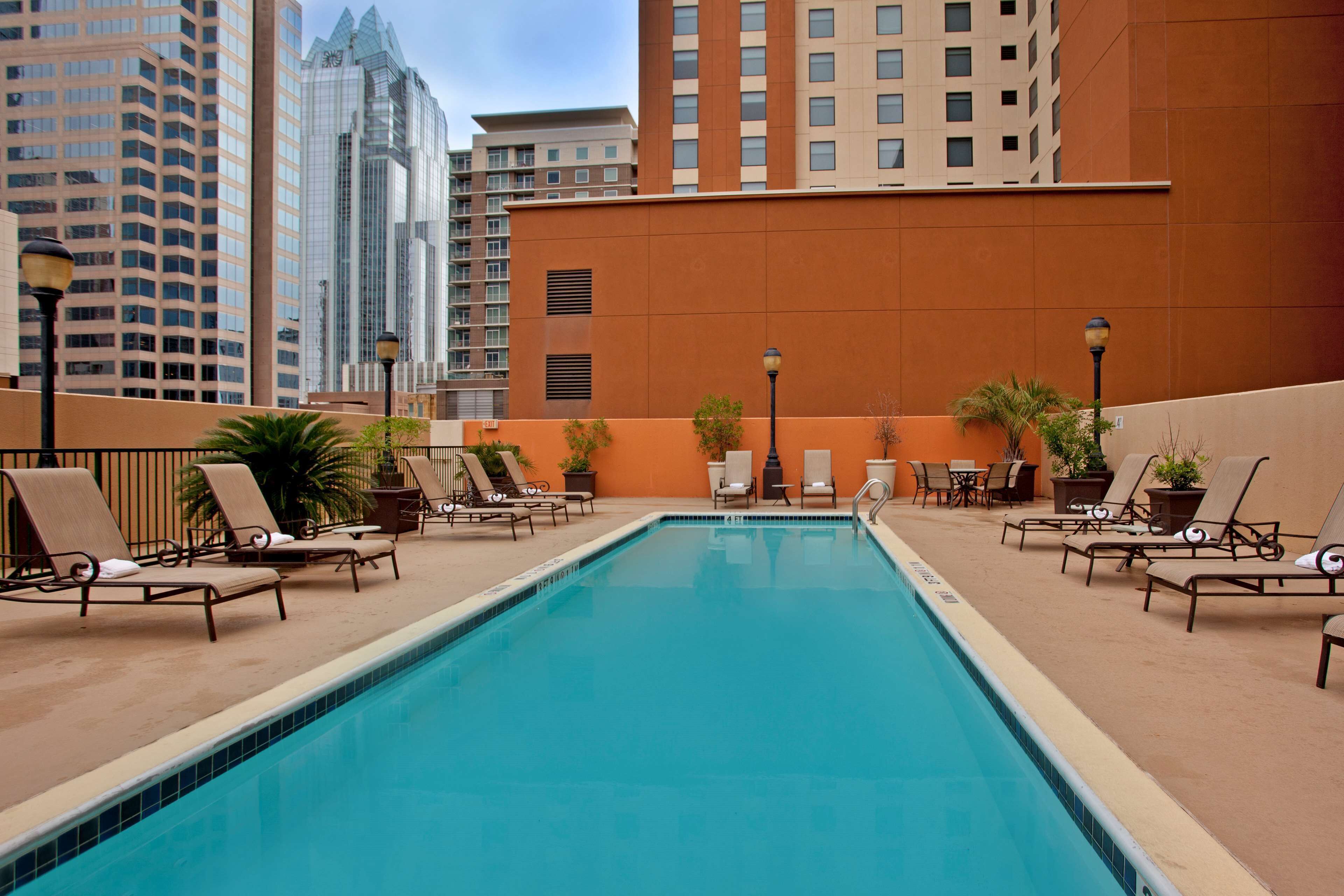 A swimming pool with lounge chairs and potted plants, surrounded by high-rise buildings.