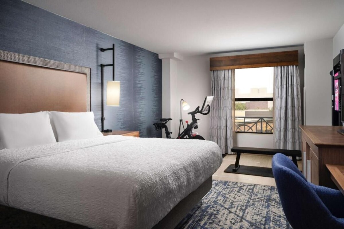 A hotel room with a large bed, a desk, a chair, a bicycle, and a balcony with a view.