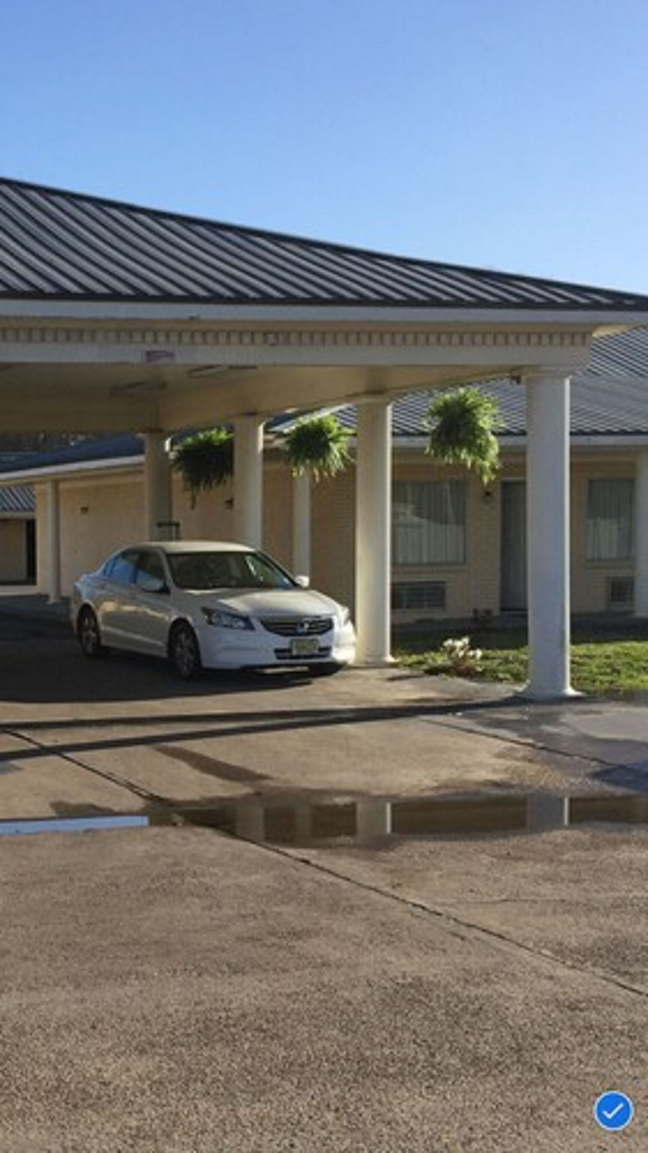 A white car parked under a covered area with columns and a sloped roof.