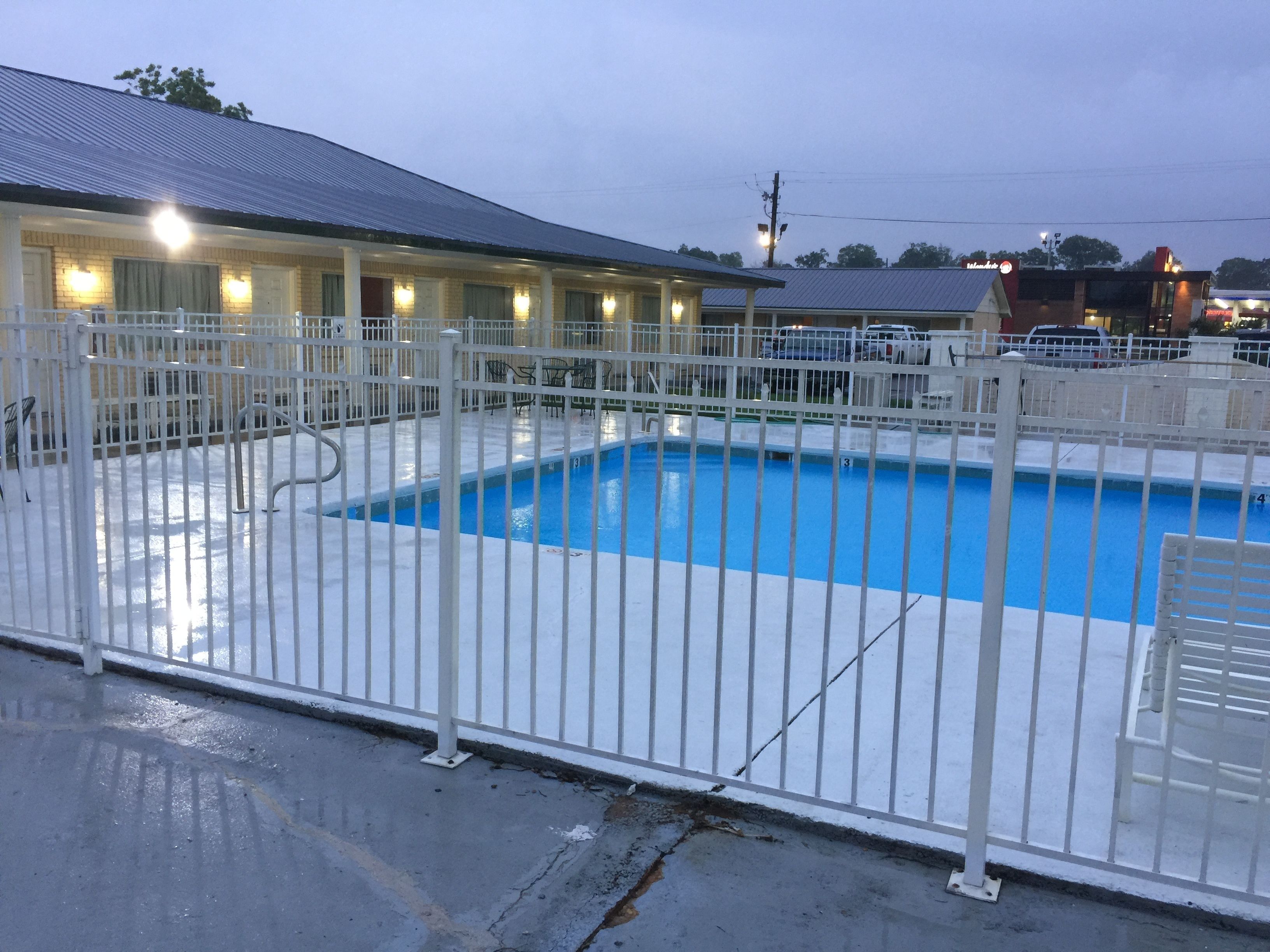 A swimming pool with a white fence, a covered area with lights, and a building in the background.