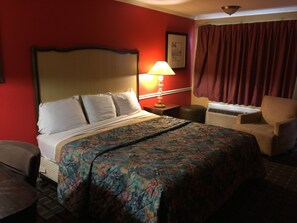 A hotel room with a bed, a chair, a lamp, and a window with curtains.