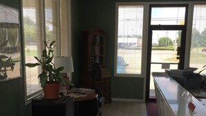 Ein Zimmer mit Schreibtisch, Stuhl, Bücherregal und einem Fenster mit Jalousien.