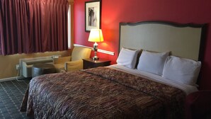 Ein Hotelzimmer mit einem großen Bett, einem Sessel, einem Schreibtisch mit Lampe und einer Wand-Klimaanlage.