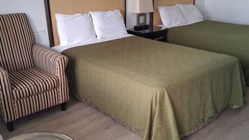 A hotel room with two single beds, a striped armchair, a bedside table with a lamp, and a glass table.