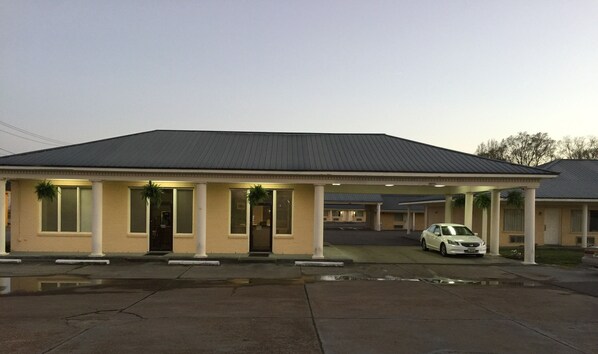 A motel with a single-story structure, a covered parking area, and a white car parked in front.