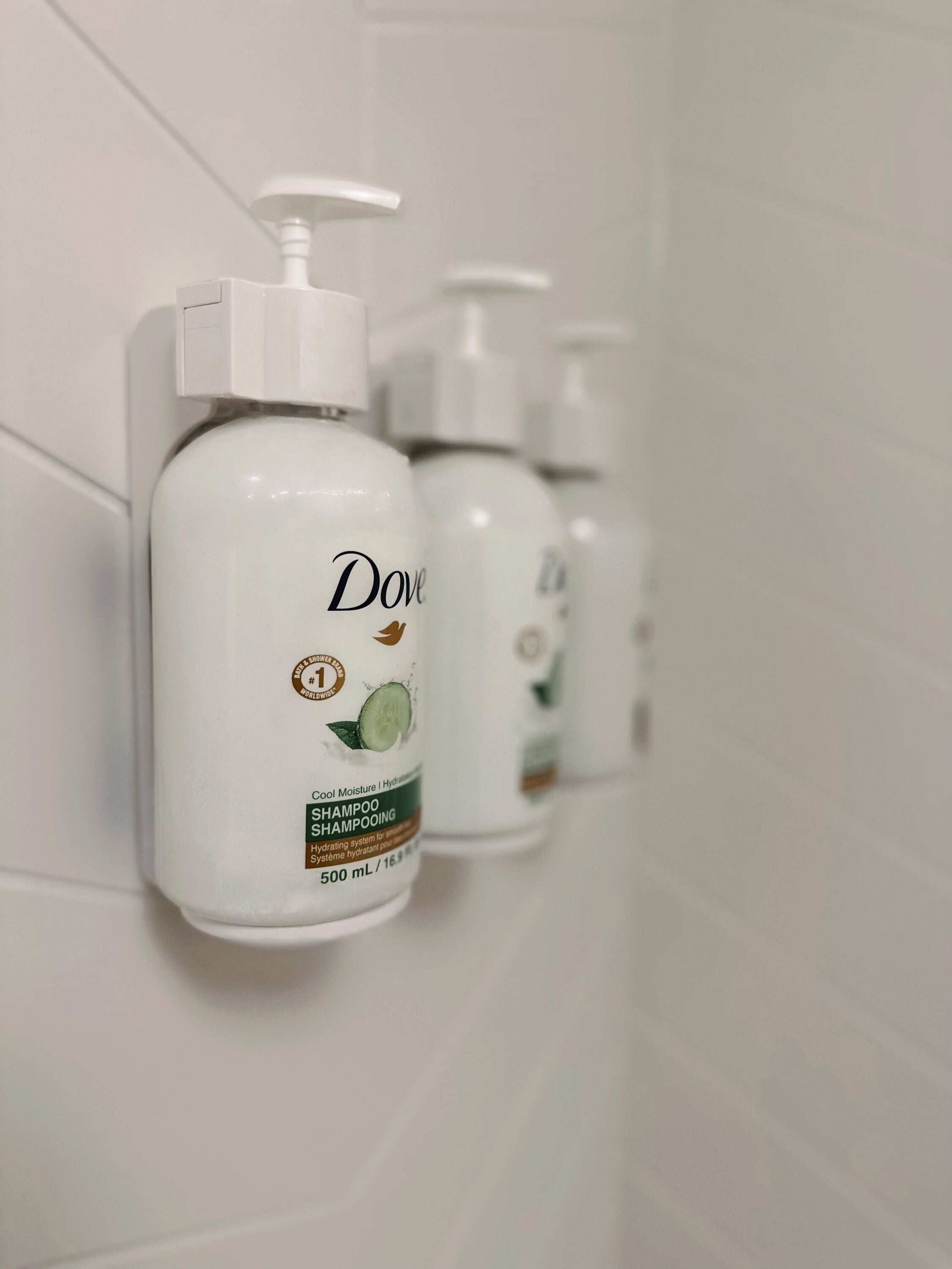 Drei Dove Shampoo-Flaschen an einer weißen Fliesenwand angebracht.