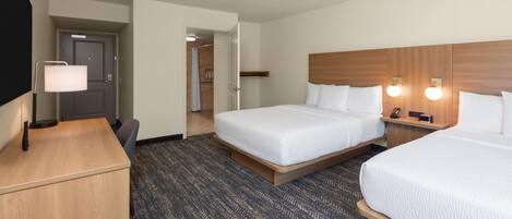 A hotel room with two beds, a desk, a lamp, and a shower area.
