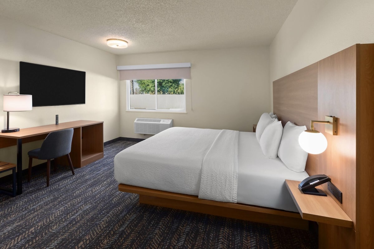 A hotel room with a bed, desk, chair, and a wall-mounted lamp.