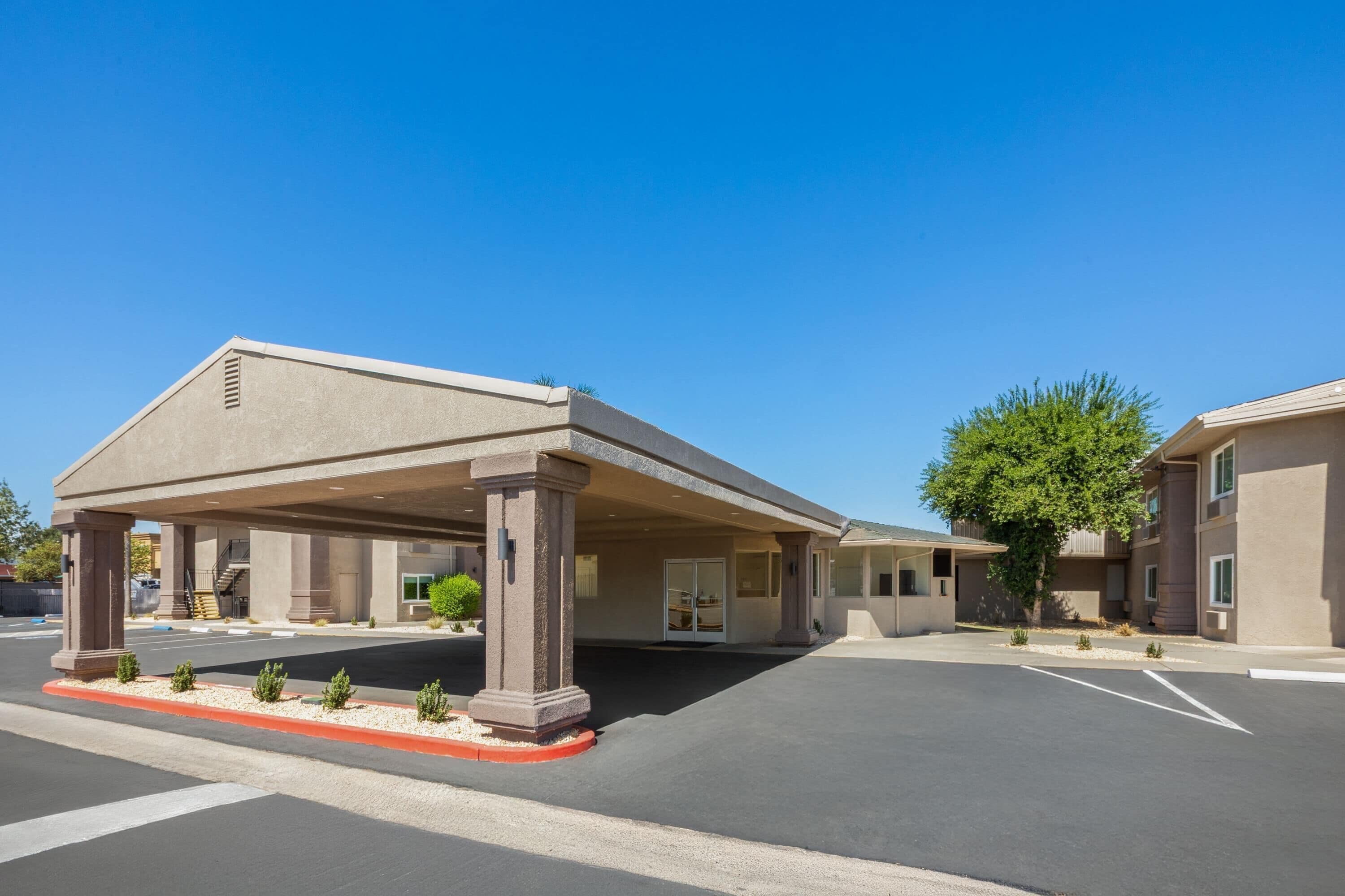 A hotel with a covered entrance, a parking lot, and a building with a flat roof.