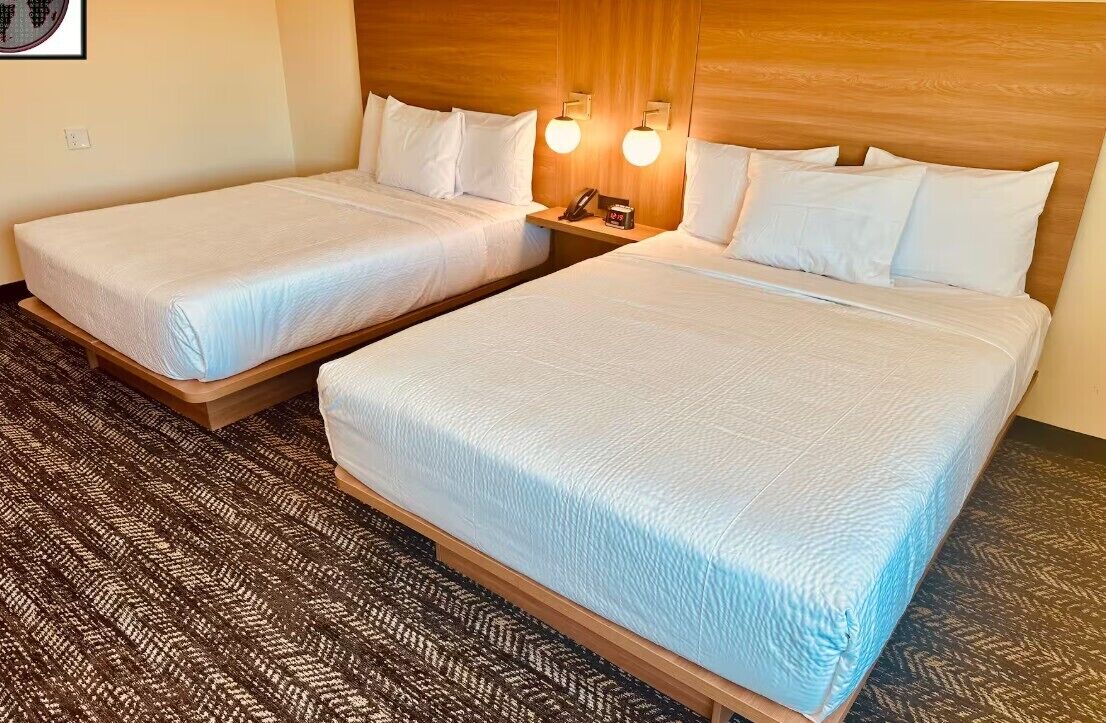 A hotel room with two beds, a wooden headboard, a patterned carpet, and a wall-mounted phone.