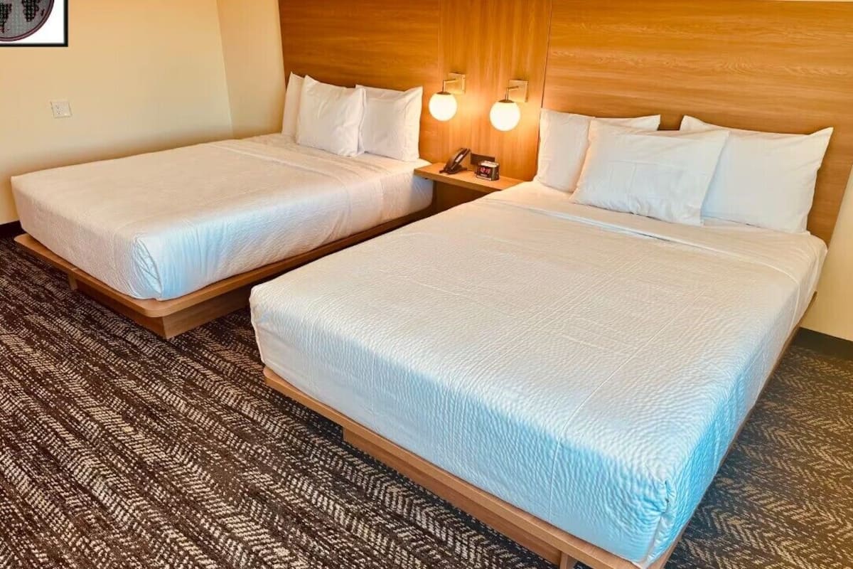 A hotel room with two beds, a wooden headboard, a patterned carpet, and a wall-mounted phone.