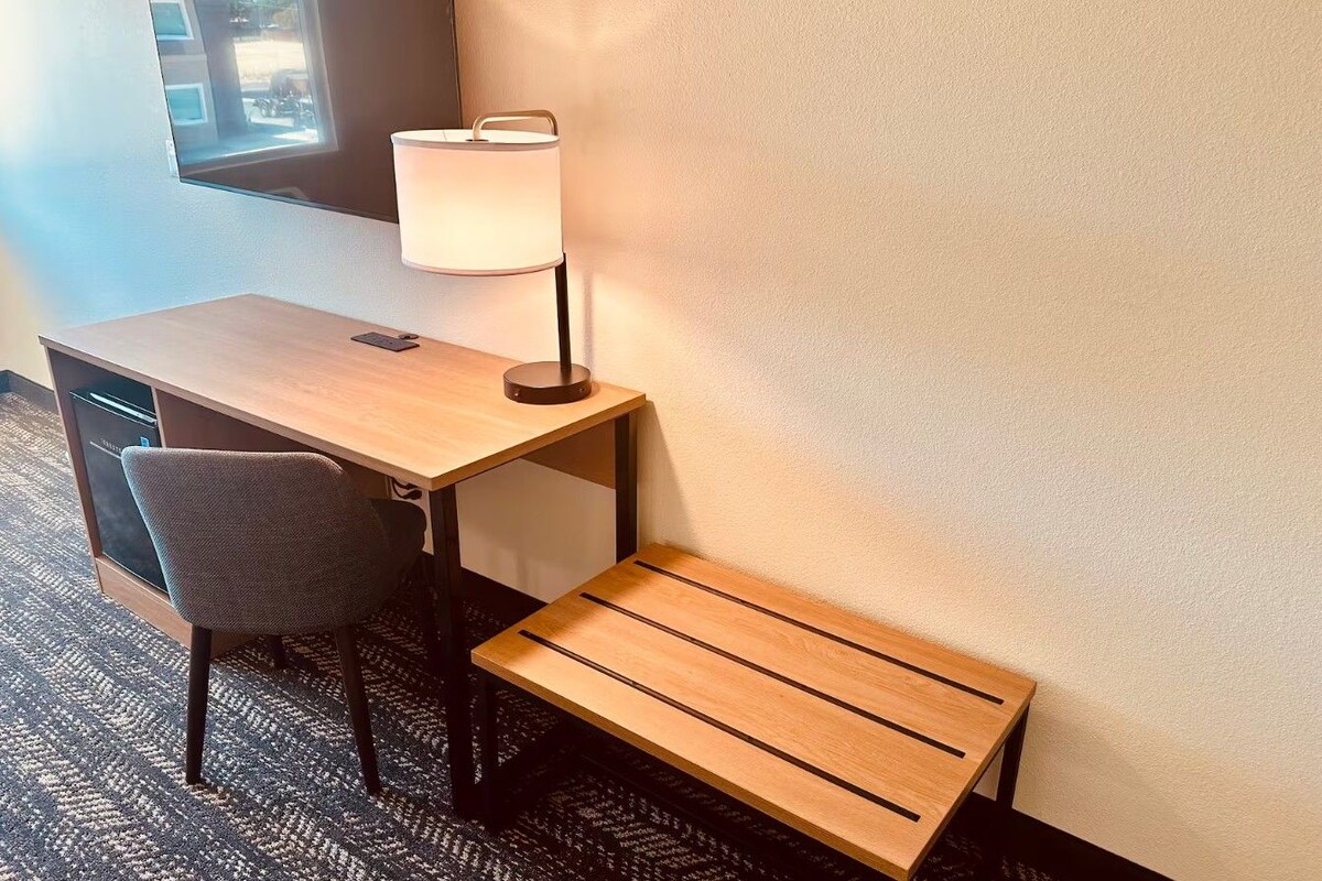 Una habitación de hotel con escritorio, silla y un pequeño banco de madera.