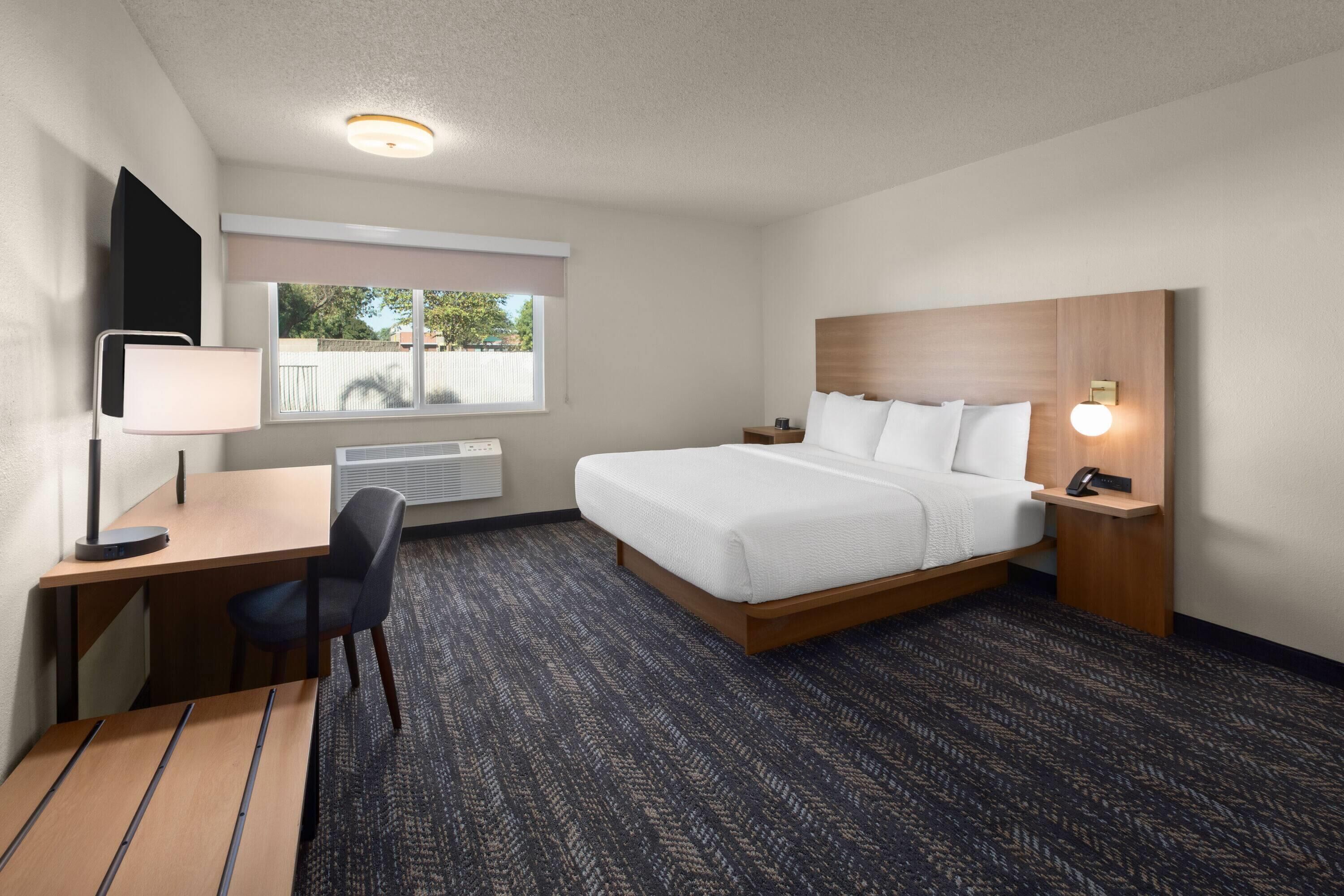 A hotel room with a bed, desk, chair, and a window with a view.