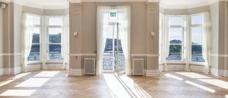 A spacious room with large windows, a view of a river, and a door leading to an outdoor balcony.