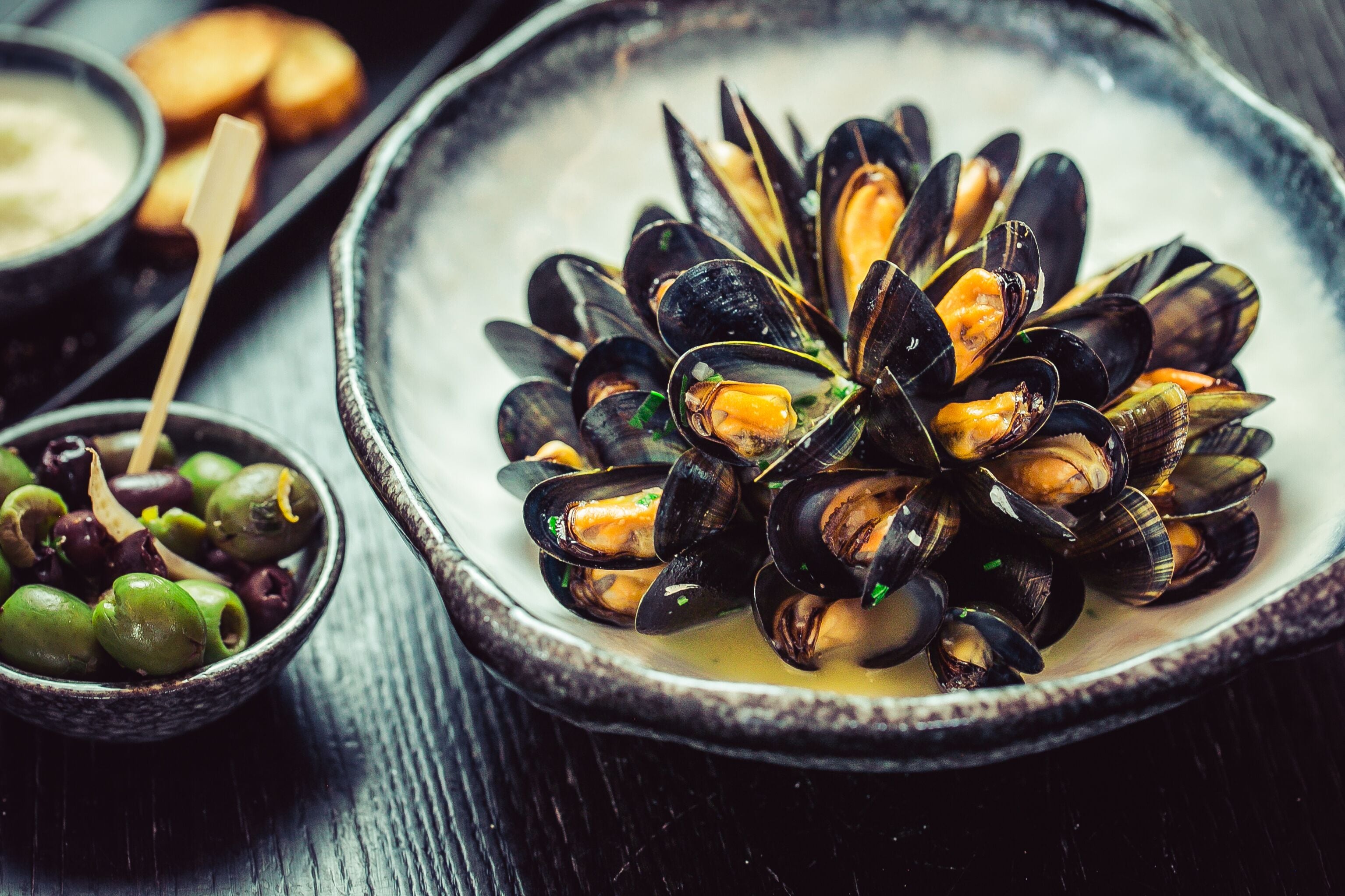 A bowl of mussels with a side of olives.