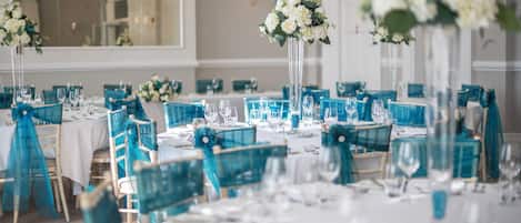 A banquet hall with tables set for a formal event, featuring teal chairs and white tablecloths.