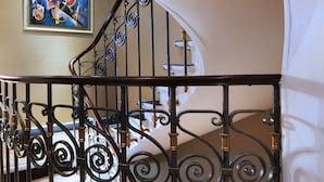A staircase with ornate black metal railings and a painting on the wall.