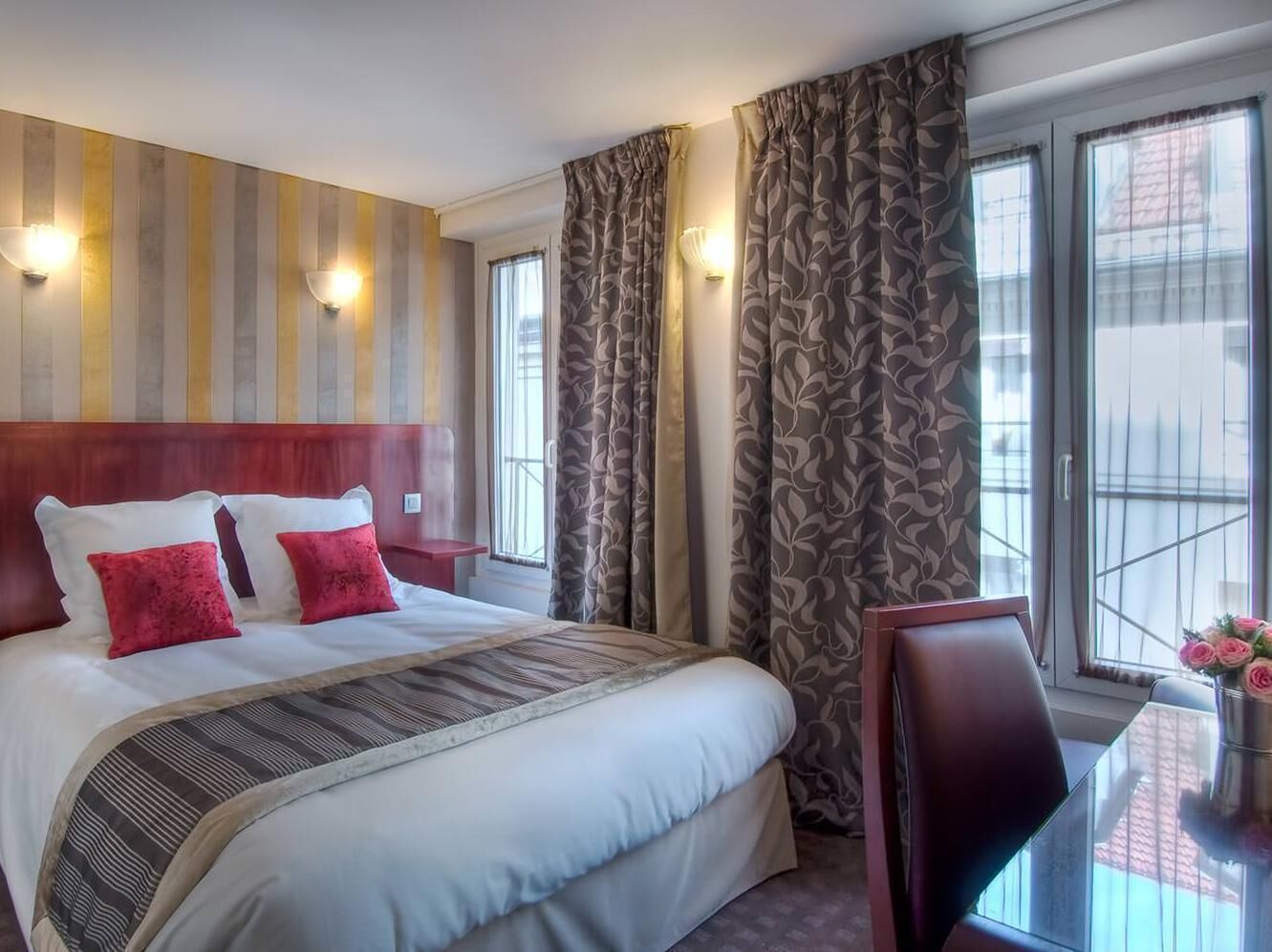 A hotel room with a large bed, a desk, two wall-mounted lights, and a window with curtains.