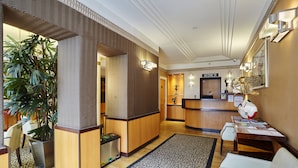 A hotel lobby with a reception desk, seating area, and a large potted plant.