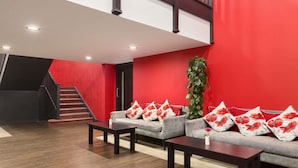 A modern living room with a grey sofa adorned with red floral pillows, a dark wooden coffee table, and a tall green plant. A staircase with a dark railing is visible in the background. - Ramada by Wyndham Oxford (Oxford)