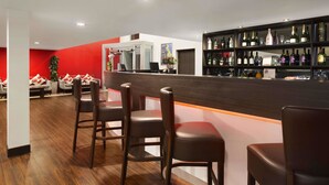 A modern bar area with a wooden counter, bar stools, and a wine rack filled with bottles. - Ramada by Wyndham Oxford (Oxford)