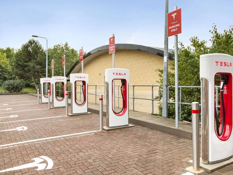 A Tesla charging station area with multiple charging points and a parking sign indicating Tesla-only parking.
