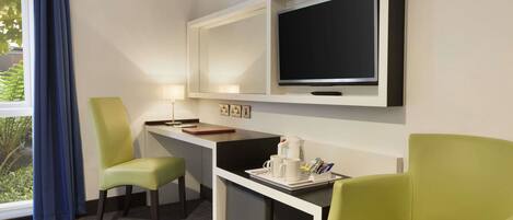 A hotel room with a desk, two chairs, a TV, and a window with curtains.