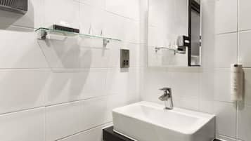 Une salle de bain moderne avec des carreaux blancs, un lavabo blanc, une étagère en verre et un miroir.