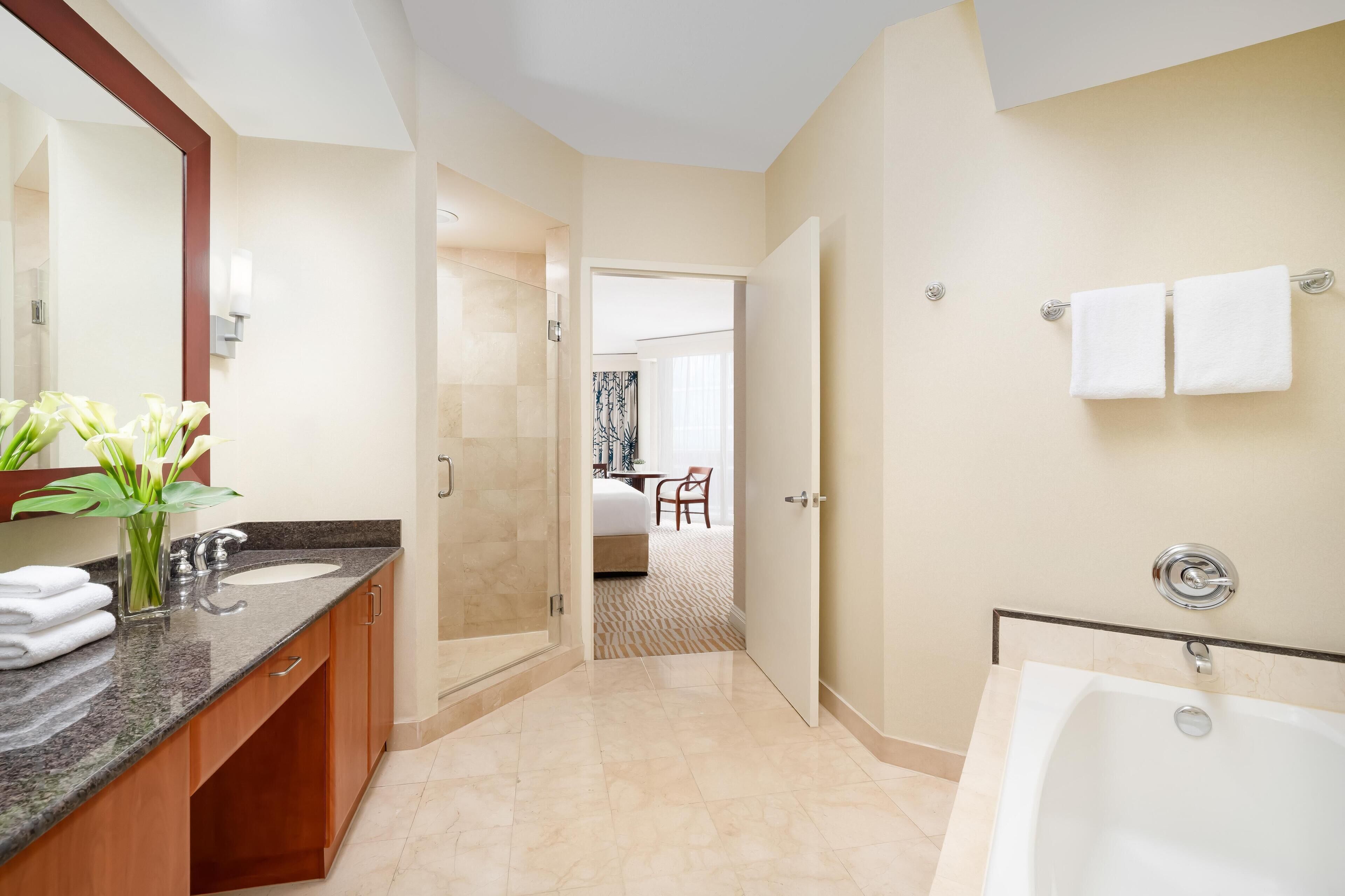 A modern hotel bathroom with a large mirror, a bathtub, and a shower area.