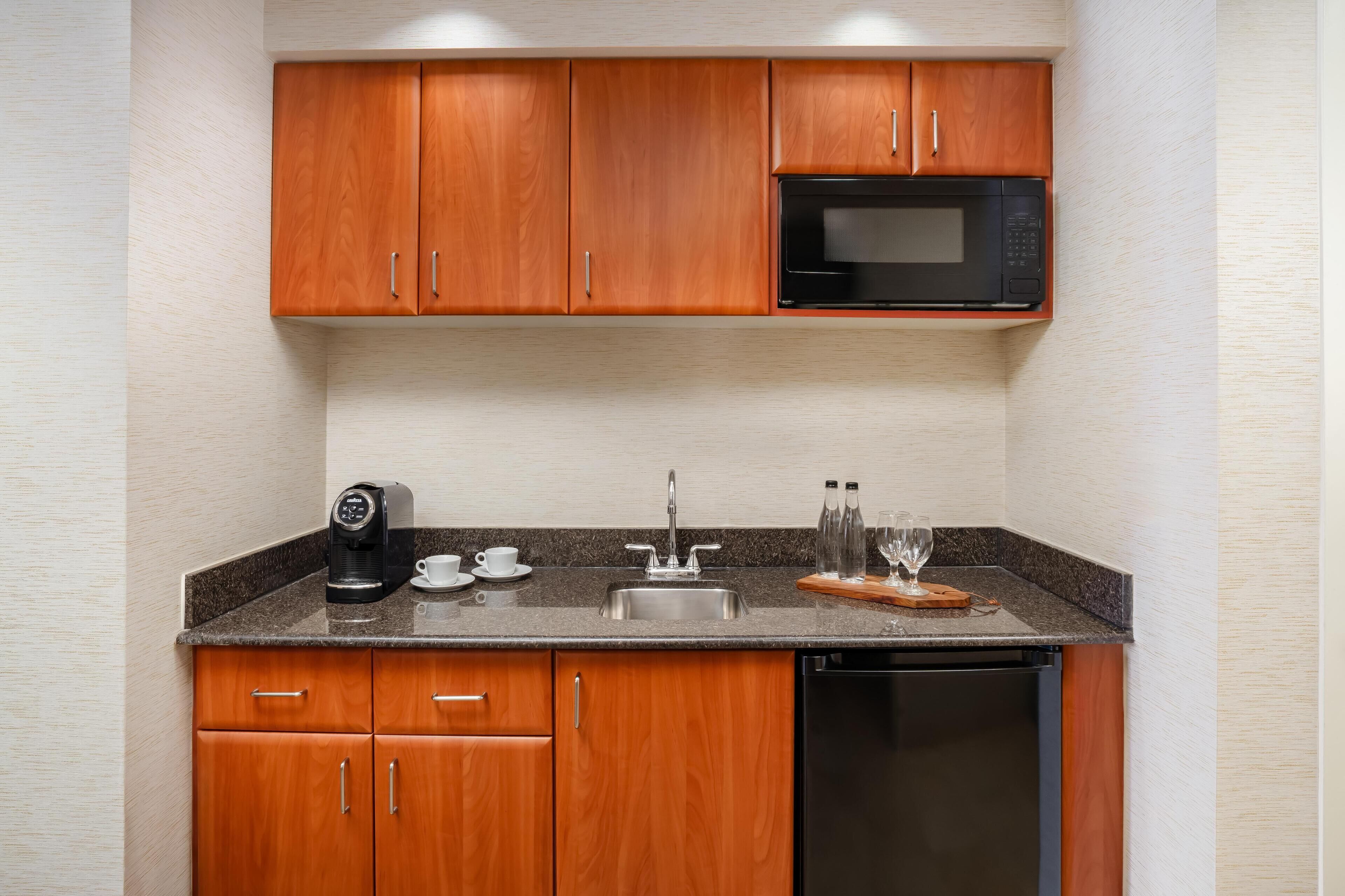 Una cocina compacta con armarios de madera, un microondas negro, una cafetera, un lavamanos y un lavavajillas.