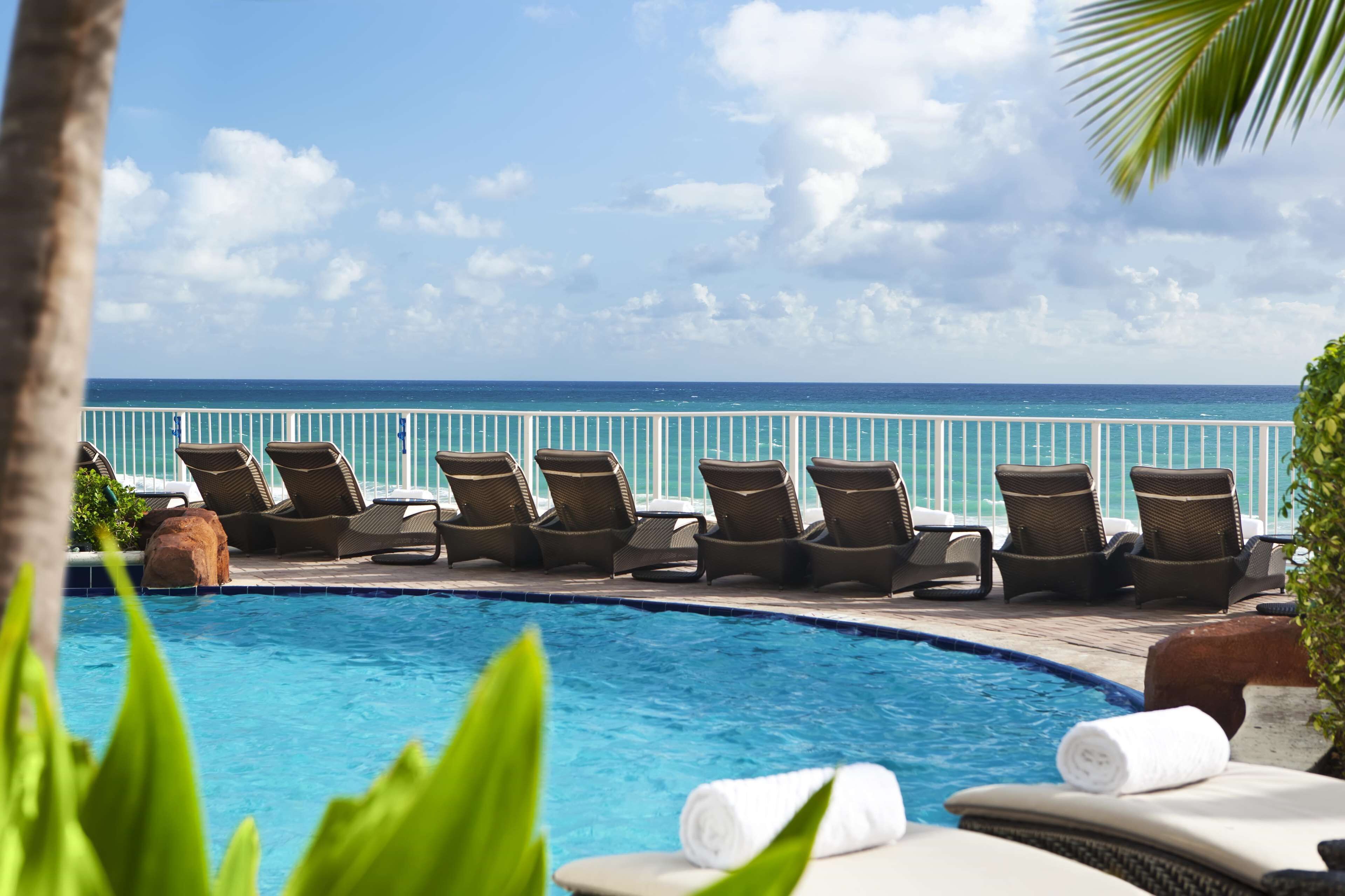 Un espace aménagé au bord de la piscine, avec des chaises longues et une vue sur l’océan.