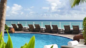 Un espace aménagé au bord de la piscine, avec des chaises longues et une vue sur l’océan.